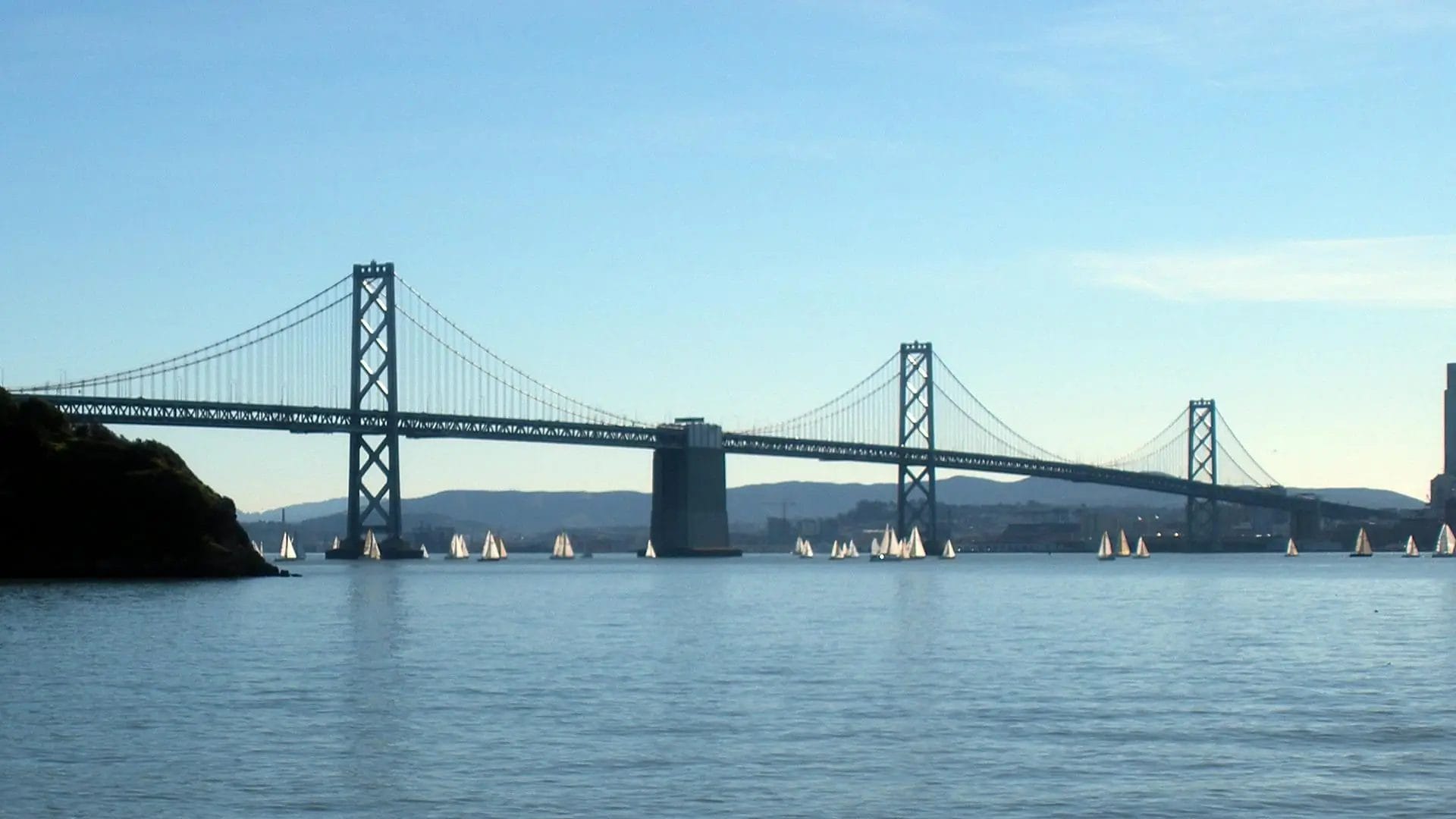 View of the san francisco bay bridge surrounded by sail boats.