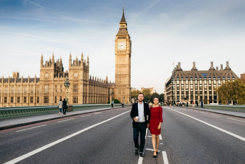 Couple hold hands walking on Westmisnter bridge with Big Ben in the background.