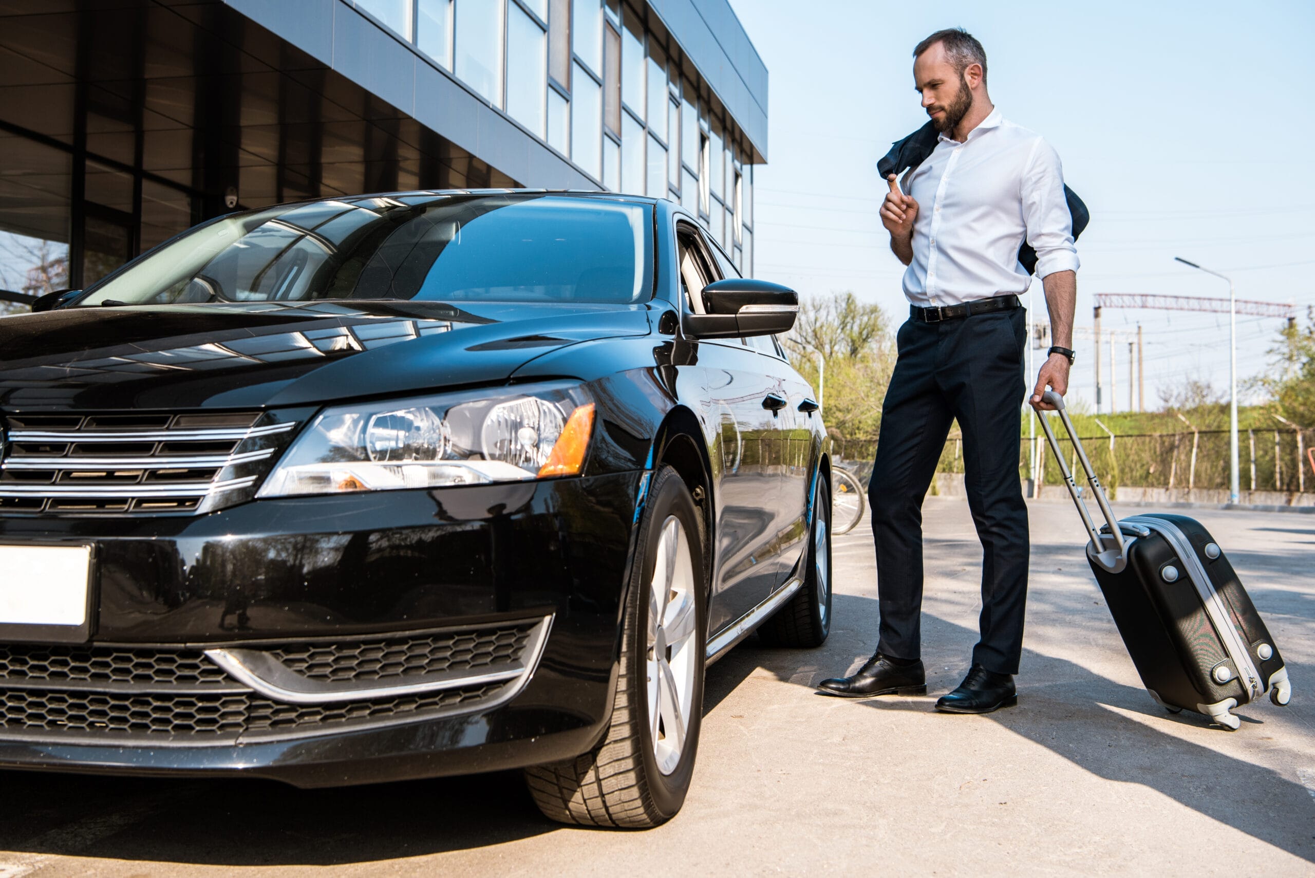 Businessman standing near black car with luggage.